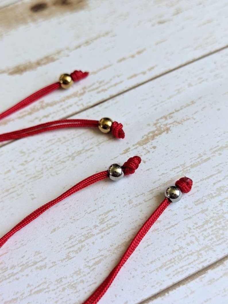May include: Three red cords with gold and silver beads at the ends. The cords are knotted at the ends with the beads.