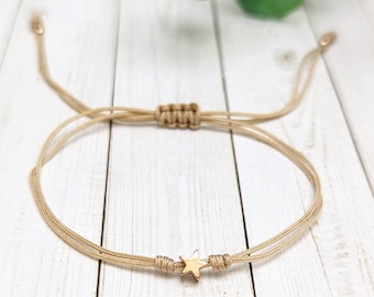 May include: A simple beige string bracelet with a gold star charm. The bracelet is adjustable and can be worn on the wrist or ankle.