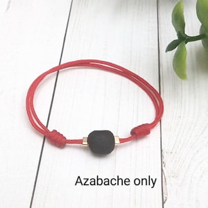 May include: A red string bracelet with a black azabache bead and gold accents.  Azabache only.