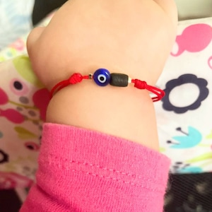 May include: Red string bracelet with a blue evil eye charm and black beads.