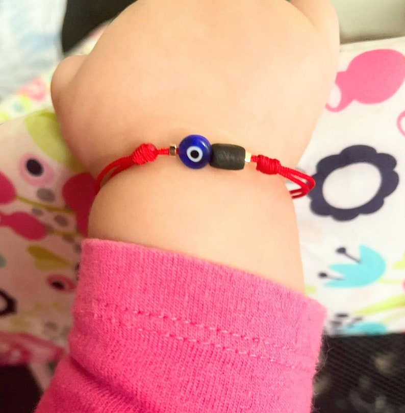 May include: Red string bracelet with a blue evil eye charm and black beads.