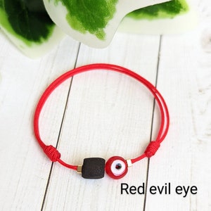May include: Red string bracelet with a black bead and a red evil eye charm. "Red evil eye" is written below the bracelet.