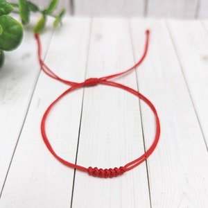 May include: A red string bracelet with a knotted design. The bracelet is tied in a simple knot and is made of a thin, red string.