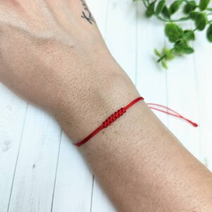 May include: A red string bracelet with a knotted design. The bracelet is tied around a person's wrist.