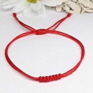 May include: A red string bracelet with a knotted design. The bracelet is made of a thin, durable cord and is adjustable to fit most wrists.