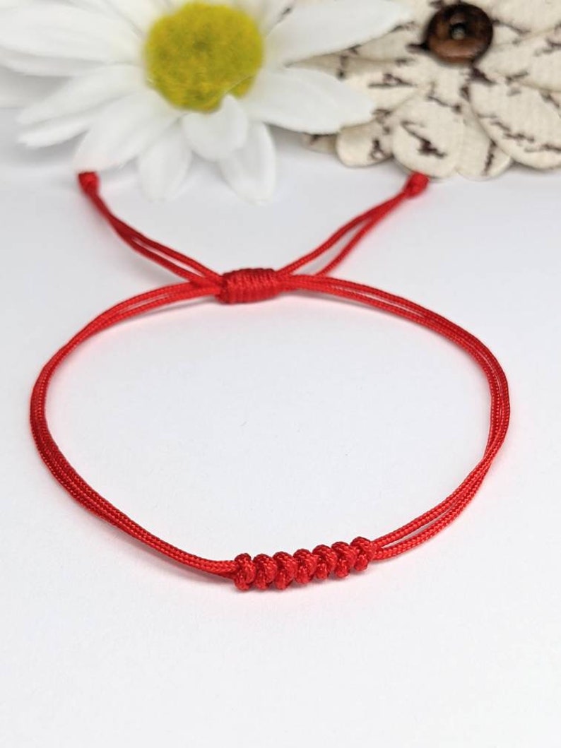 May include: A red string bracelet with a knotted design. The bracelet is made of a thin, durable cord and is adjustable to fit most wrists.