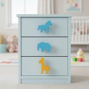 May include: A light blue three-drawer cabinet with animal-shaped drawer pulls. The top drawer has a blue horse, the middle drawer has a blue elephant, and the bottom drawer has a yellow giraffe. The cabinet is in a nursery setting.