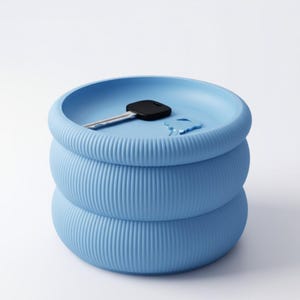 May include: A light blue, cylindrical storage container with a ribbed, textured exterior and a recessed top surface. A single metal key with a black plastic head rests inside the top basin of the container, which serves as a small tray.