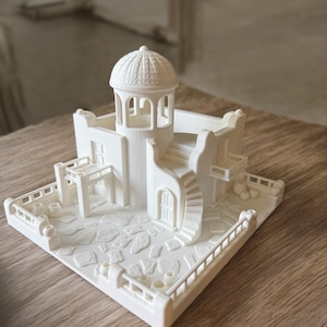 May include: A 3D-printed miniature model of a white building with a domed roof, spiral staircase, and detailed architectural features. The model includes a courtyard with textured paving stones and a surrounding railing.