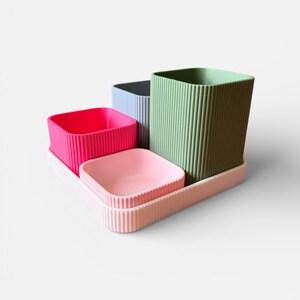 May include: A set of four colourful, ribbed containers on a tray. The containers are square-shaped and come in pink, light pink, blue, and green. The tray and containers have a vertical ribbed design.