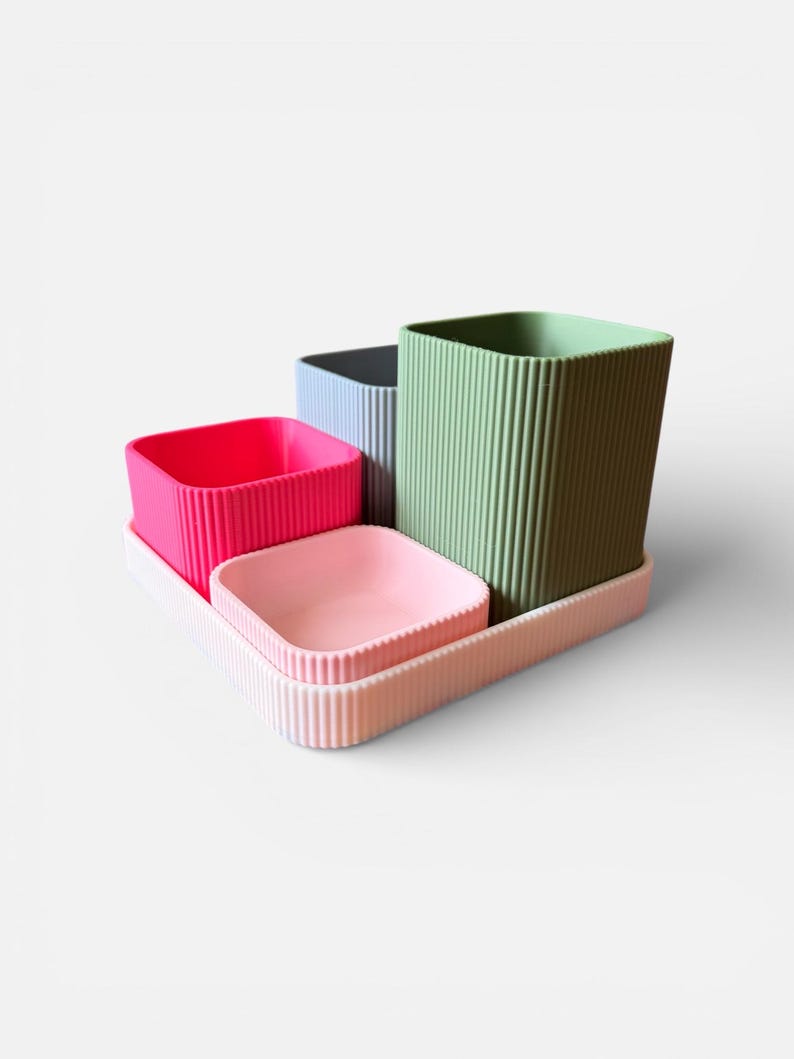 May include: A set of four colourful, ribbed containers on a tray. The containers are square-shaped and come in pink, light pink, blue, and green. The tray and containers have a vertical ribbed design.