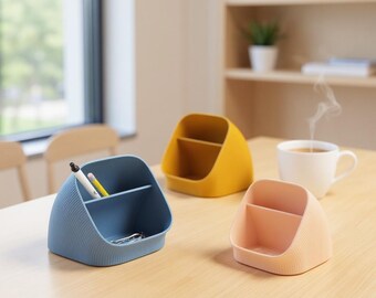 May include: Three small, colorful desk organizers in blue, yellow, and peach. Each organizer has a divided interior. A white mug of coffee sits on the table. Pens and pencils are in the blue organizer.