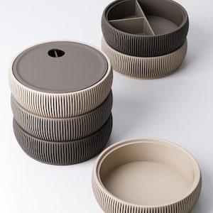 May include: A stack of round, ribbed storage containers in shades of brown and beige. One container has a lid with a small hole, while another is divided into three sections. The containers are designed for organizing and storage.