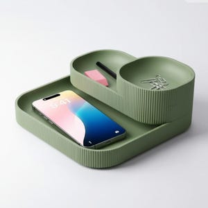 May include: A sage green desk organizer with a ribbed texture. It features a square base with a smartphone, a smaller tray with a pencil and eraser, and a round compartment with paper clips. The phone displays the time 9:41.