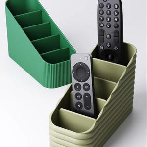 May include: Two slanted, ribbed storage organizers with four internal compartments each. One organizer is a vibrant green, while the other is a muted sage green. A black television remote and a grey streaming device remote are placed inside.