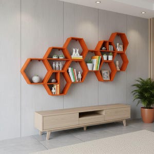 May include: A wall-mounted orange honeycomb shelving unit composed of multiple hexagonal compartments. The shelves hold various items including small potted plants, books, white figurines, and framed pictures, arranged across the connected structure.