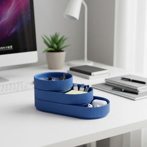 May include: A three-tiered, blue desk organizer with a ribbed texture. The organizer holds office supplies like paper clips, USB drives, sticky notes, and earbuds. The desk is white, with a computer, lamp, and plant in the background.