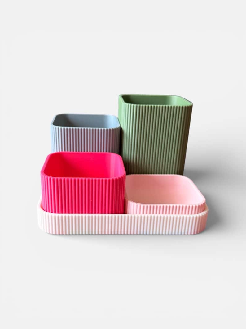 May include: A collection of four colourful, ribbed containers in shades of pink, green, blue, and a light pink tray. The containers are square or rectangular and vary in size, with vertical ribbing on the sides.