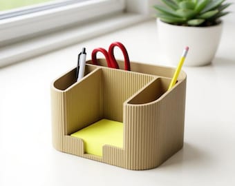 May include: A beige desk organizer with multiple compartments. It holds a pen, red scissors, a yellow pencil, and a pad of yellow sticky notes. The organizer has a ribbed texture and is designed for office or home use.