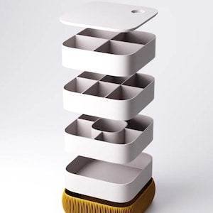 May include: A modular storage organizer with a mustard yellow ribbed base and four stacked white trays. Each tray features different internal compartment configurations, including square and rectangular sections, topped with a flat white lid.
