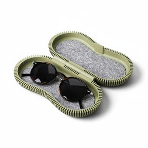 May include: An open, oval-shaped sage green glasses case with a ribbed exterior and a grey felt interior lining. Inside the case rests a pair of round, dark-tinted sunglasses with a tortoiseshell-patterned frame and thin silver-toned metal temples.