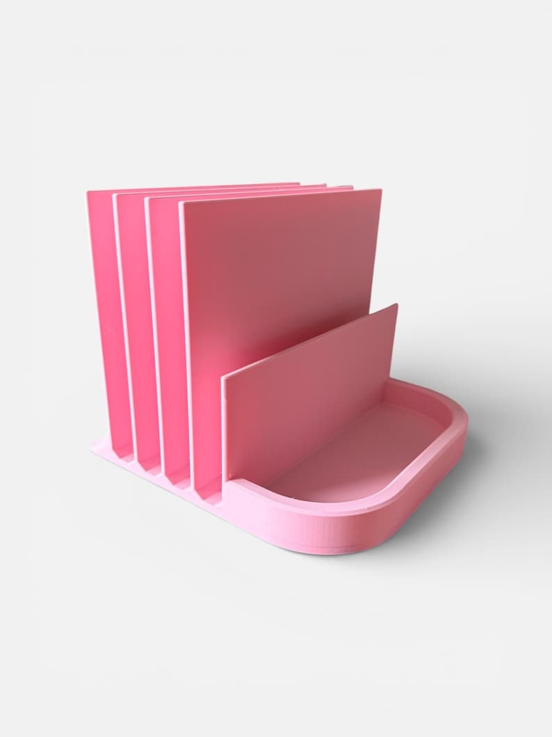 May include: A pink desk organizer with a tray and vertical dividers. The organizer has a rectangular base with a curved front and a series of upright dividers to hold papers or files. The color is a solid, soft pink.