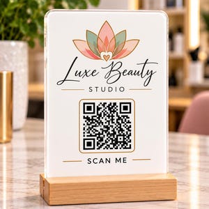 May include: A rectangular acrylic sign with a light wood base featuring a pink and green lotus flower logo, the text Luxe Beauty STUDIO, a black and white QR code, and the text SCAN ME printed in black on a white background.