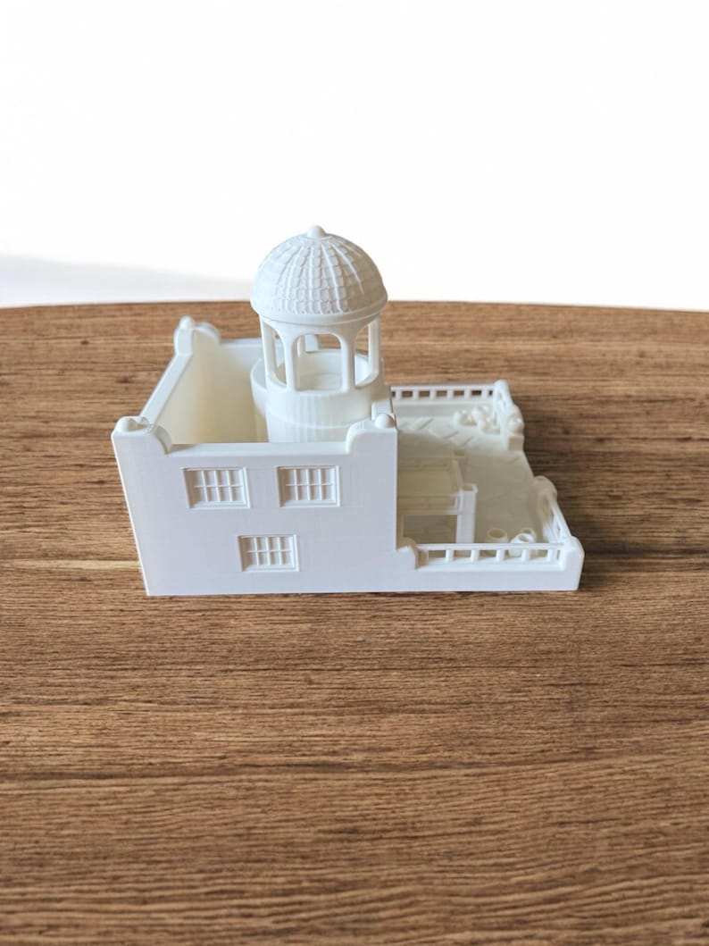 May include: A white miniature architectural model of a building with a domed gazebo, windows, and a balcony. The model is made of a solid white material and sits on a wooden surface.