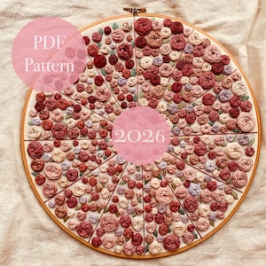 Può includere: Ricamo floreale circolare con numerose rose rosse, rosa e crema. Il testo "PDF Pattern" e "2026" è sovrapposto all'immagine. Il ricamo è racchiuso in un cerchio di legno.