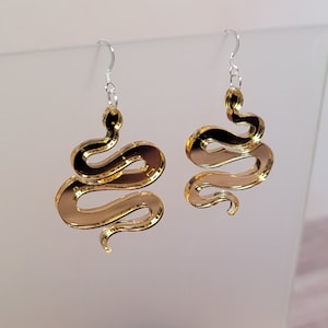 May include: Gold mirrored snake earrings with silver hooks. The snake is curled in a S shape.