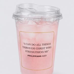 Puede incluir: Un vaso de plástico transparente lleno de una bebida rosa y hielo, cubierto con una tapa transparente. El vaso tiene una etiqueta con borde dorado con el texto "I CAN DO ALL THINGS THROUGH CHRIST WHO STRENGTHENS ME." y "PHILIPPIANS 4:13."