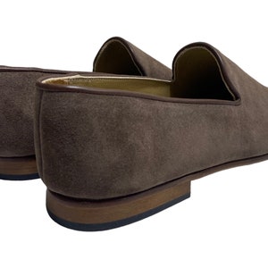 May include: A pair of brown suede loafers with a leather sole. The loafers have a pointed toe and a slip-on design.