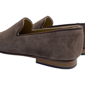 May include: A pair of brown suede loafers with a leather sole. The loafers have a pointed toe and a slip-on design.