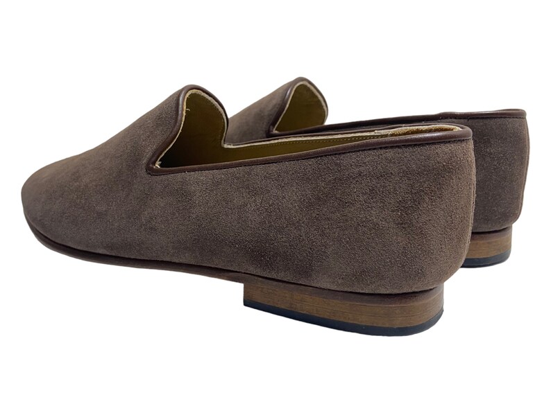 May include: A pair of brown suede loafers with a leather sole. The loafers have a pointed toe and a slip-on design.