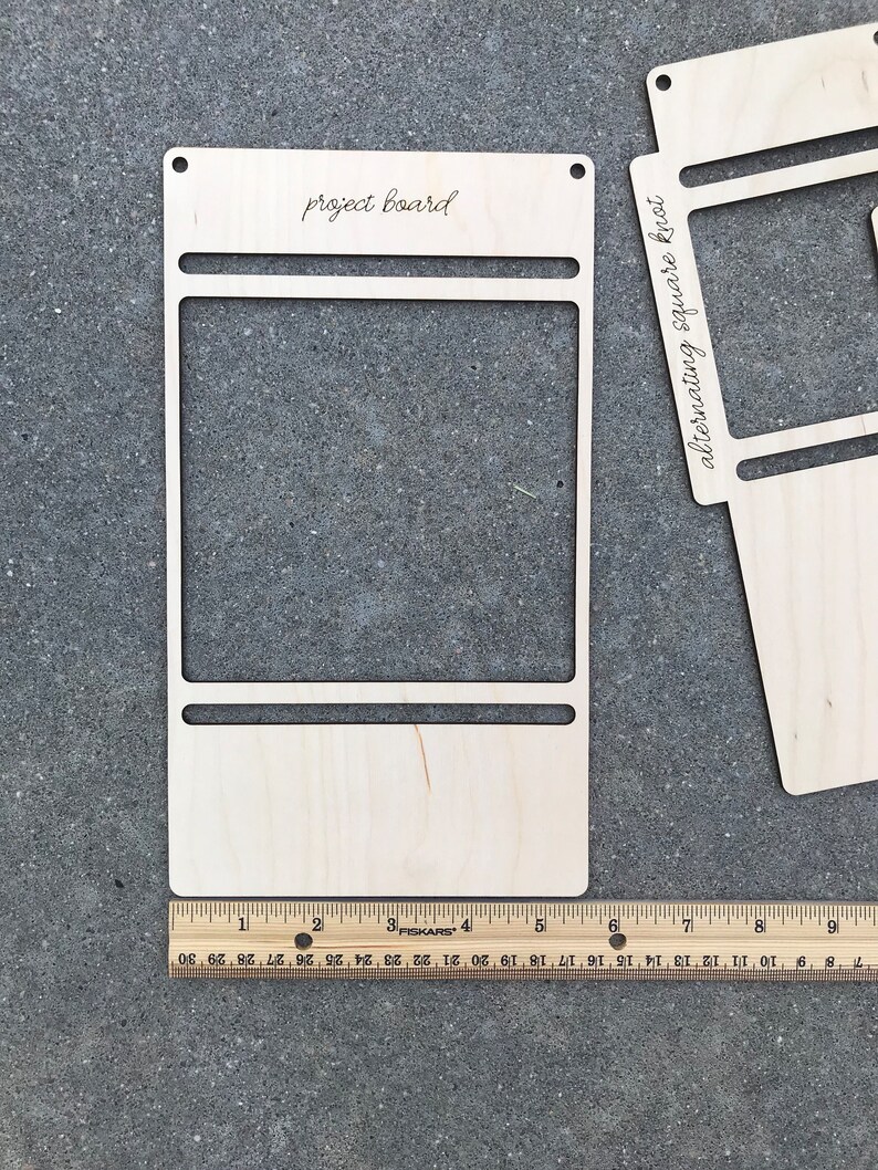 May include: A light-colored wooden project board with a rectangular cutout and horizontal slots, featuring the text 'project board' at the top. A wooden Fiskars ruler is positioned at the base, showing the board is approximately 9 inches wide.