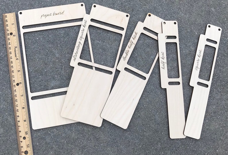 May include: Five light-colored wooden macrame boards of varying widths, each featuring cut-out slots and holes. A wooden ruler is placed on the left, showing measurements up to 11 inches. The boards are labeled with text including project board, alternating square knot, double half hitch, half knot, and square knot.
