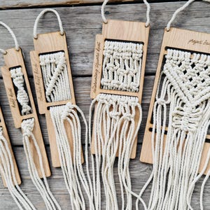 May include: Five rectangular wooden boards with hanging loops, each featuring different cream-colored macrame knot patterns. The boards are labeled with text including square knot, half knot, double half hitch, alternating square knot, and project board.