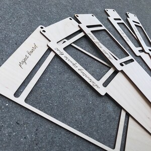 May include: A set of light-colored wooden boards with cut-out rectangular centers and small holes at the corners. The boards feature laser-engraved text including the phrases project board, alternating square knot, and double half hitch.