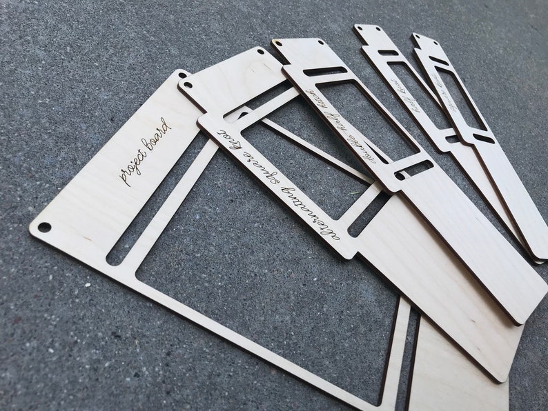 May include: A set of light-colored wooden boards with cut-out rectangular centers and small holes at the corners. The boards feature laser-engraved text including the phrases project board, alternating square knot, and double half hitch.
