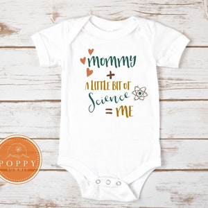May include: White baby onesie with the text "mommy + a little bit of science = me" in brown, green, and orange lettering. There are four small orange hearts above the text and an atom symbol next to the word "science".