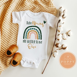 May include: White baby onesie with a rainbow design and the text "Two Mums Are Better Than One" in green and brown lettering. A heart is next to the word "Mums".