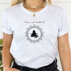 May include: A white t-shirt with the text "Pause and Reflect" and a black cat in a yoga pose inside a mandala design.