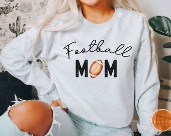 May include: A light gray crewneck sweatshirt featuring the black cursive text Football above the word MOM in black glittery block letters, with a brown and white football replacing the letter O in the center of the word MOM.