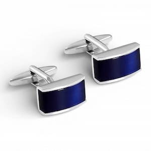 Puede incluir: Un par de gemelos plateados con un centro rectangular de esmalte azul oscuro. Los gemelos tienen un diseño clásico, con un respaldo con bisagras para una sujeción segura. La plata pulida enmarca el azul vibrante, creando un accesorio sofisticado.