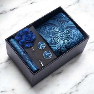 Peut inclure: Coffret cadeau bleu marine contenant une cravate à motifs cachemire, une pochette, une fleur de revers et des boutons de manchette. L'ensemble comprend une cravate, une pochette, une fleur de revers et des boutons de manchette.