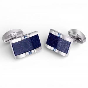 May include: A pair of silver cufflinks with rectangular, dark blue speckled insets. The insets are framed by silver and accented with small, clear and blue gemstones. The cufflinks are displayed on a white background.