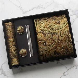 May include: A formal accessory set in a black box. The set includes a paisley patterned tie, pocket square, cufflinks, and tie clip. The paisley pattern is in shades of gold and brown.