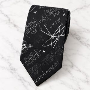 May include: A black necktie featuring a white printed pattern of mathematical trigonometric formulas, geometric diagrams, and a small illustration of the planet Saturn with rings, accented by small four-pointed stars scattered across the fabric.