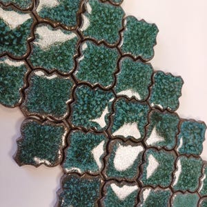 Op de afbeelding: Groene en witte keramische mozaïektegels in een vierpasvorm. De tegels hebben een gespikkelde glazuur en een licht verhoogde rand.