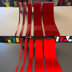 May include: Five rolls of red reflective vinyl tape. The tape is on a white grid surface. The tape is in different widths.
